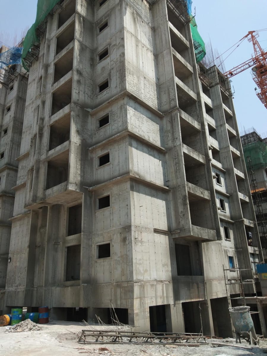 Bare concrete residential tower under construction with safety netting and a tower crane