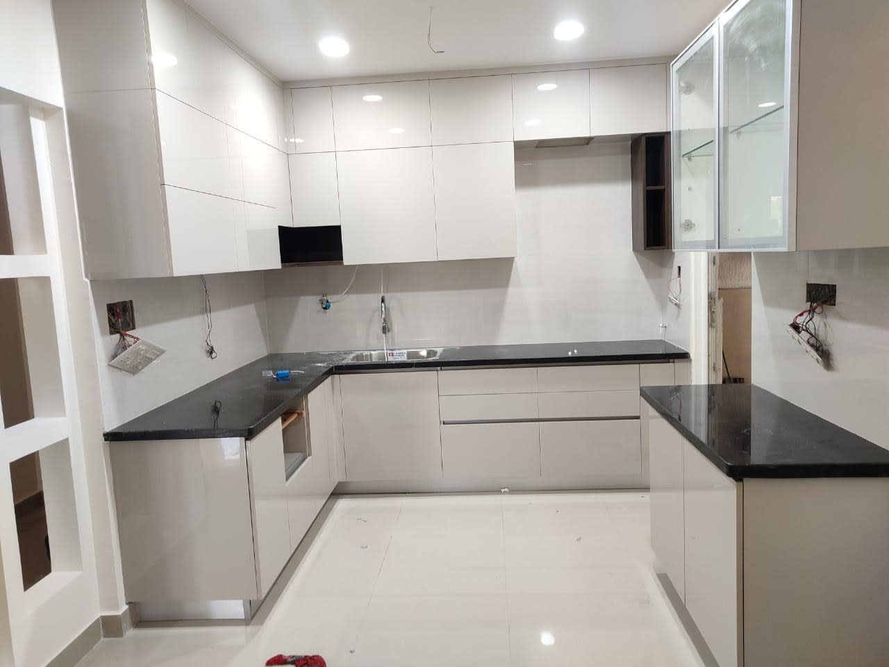Newly installed U-shaped modular kitchen with glossy white cabinets, black countertops and glass-fronted wall units