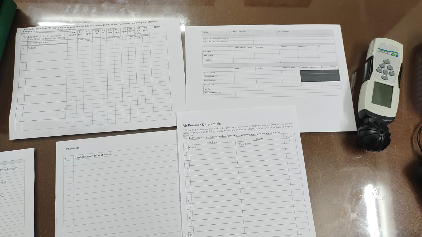 Printed air quality audit forms spread on a table next to a handheld air quality meter