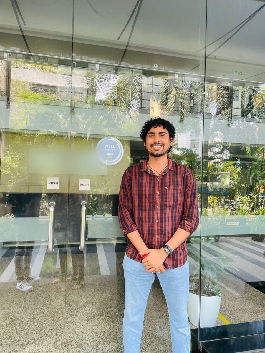 Sagar standing outside the glass entrance of an office building with a WELL Health-Safety Rated seal on the door