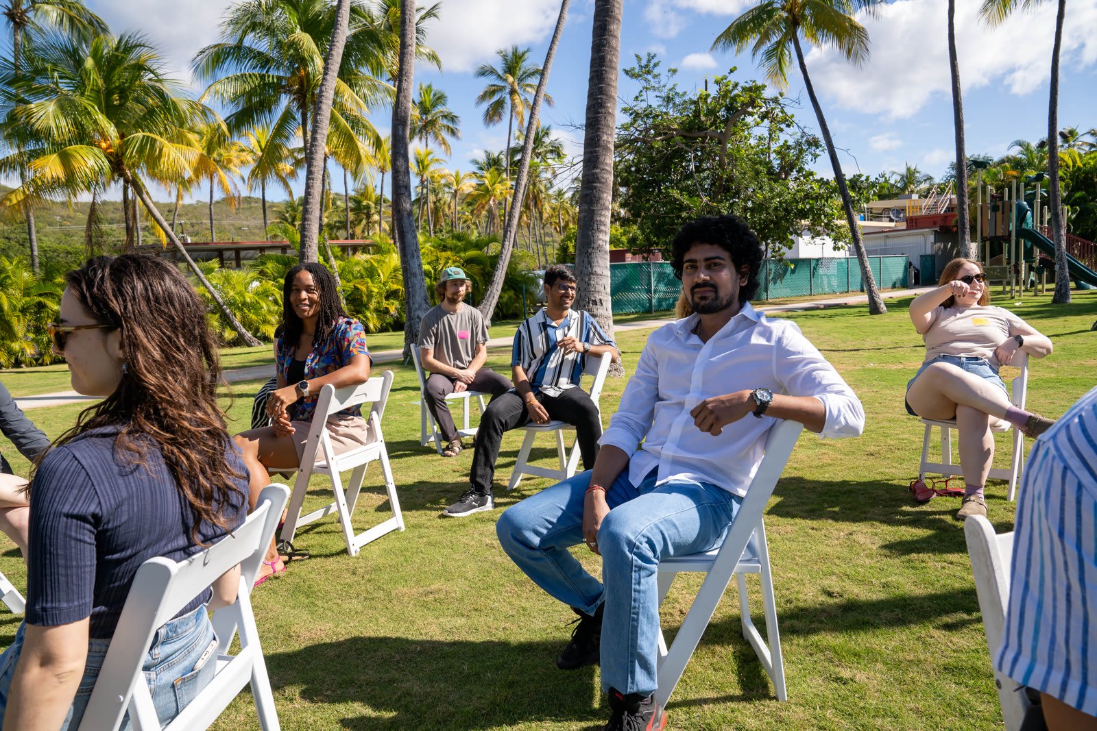 WAP Sustainability team members seated in a circle of white chairs on a lawn under palm trees