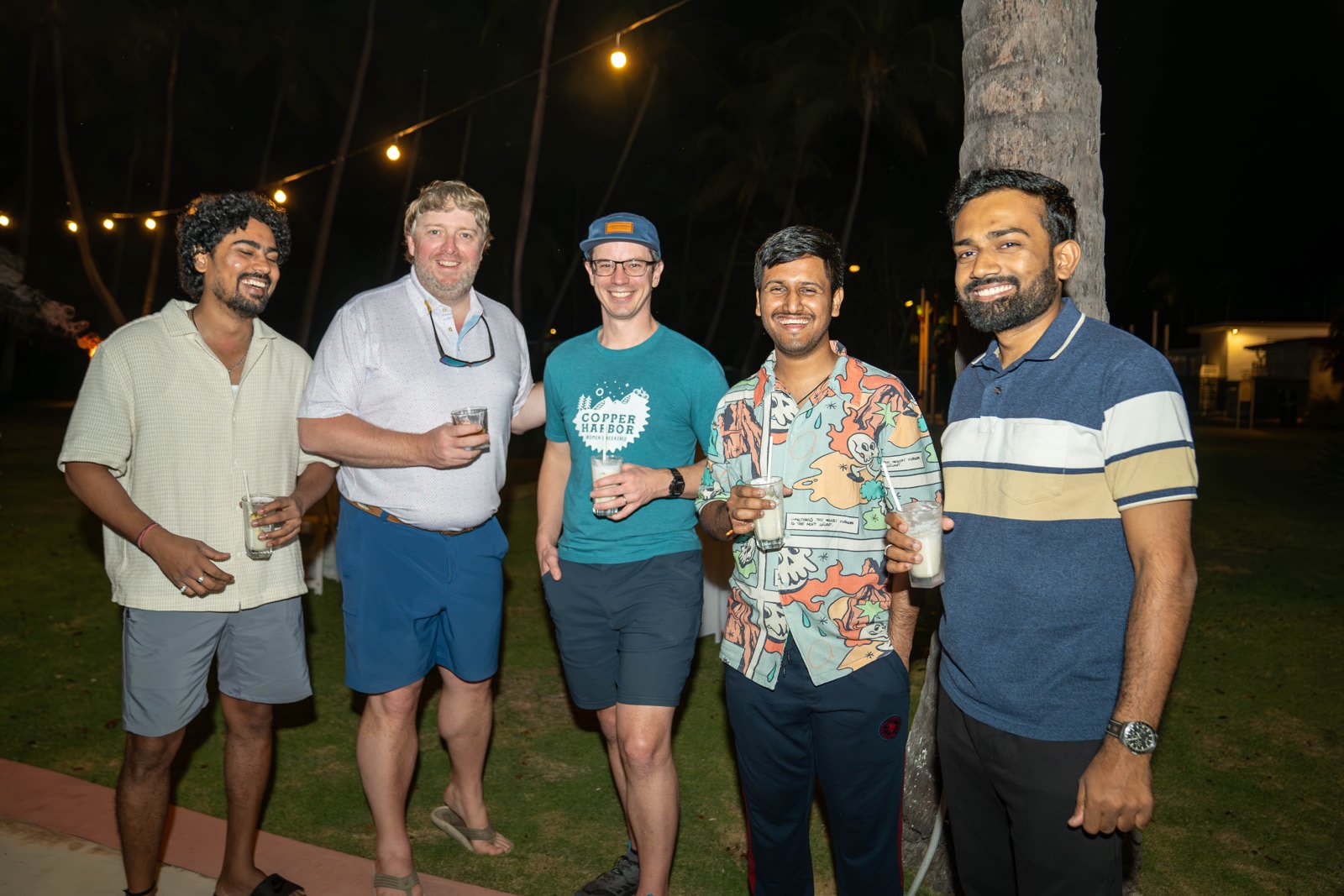 Five colleagues smiling together outdoors at night under string lights