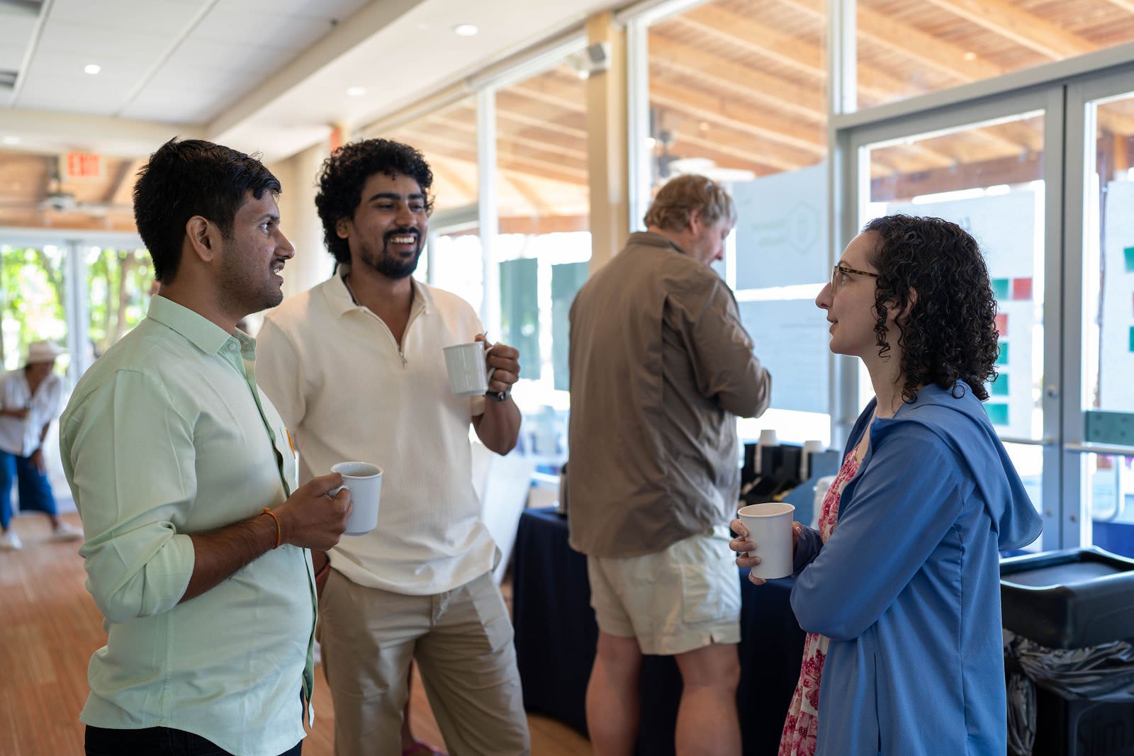 Sagar holding a coffee cup and laughing with colleagues in a bright meeting room