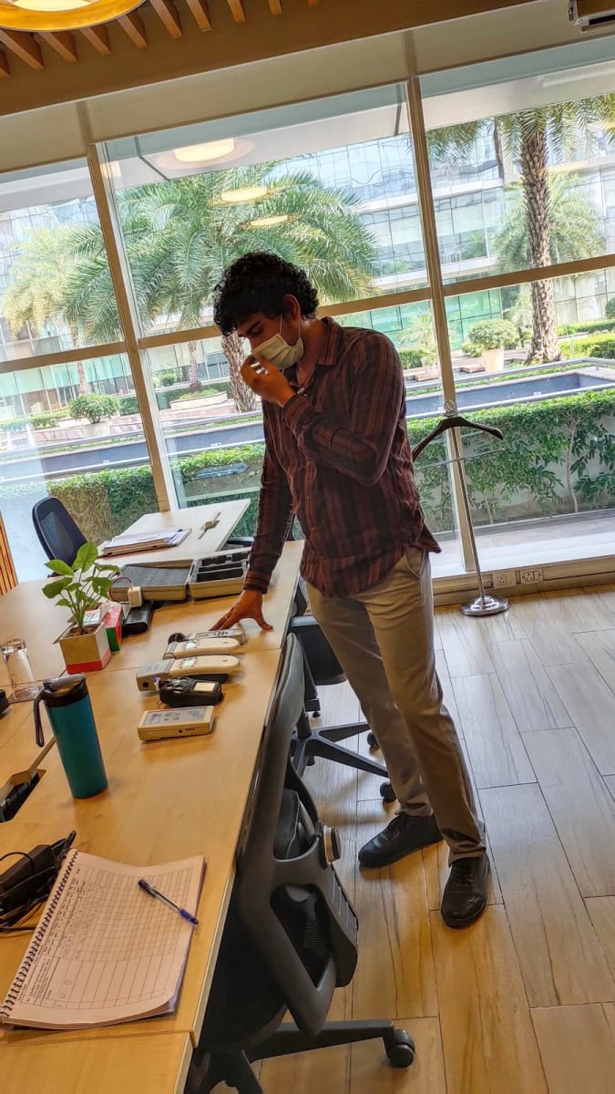 Sagar in a face mask leaning over a desk lined with handheld air quality monitors, a reading log open beside them