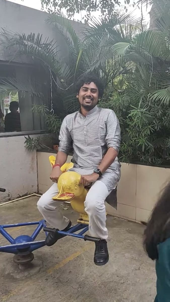 Sagar laughing while sitting on a yellow duck see-saw in a small outdoor play area