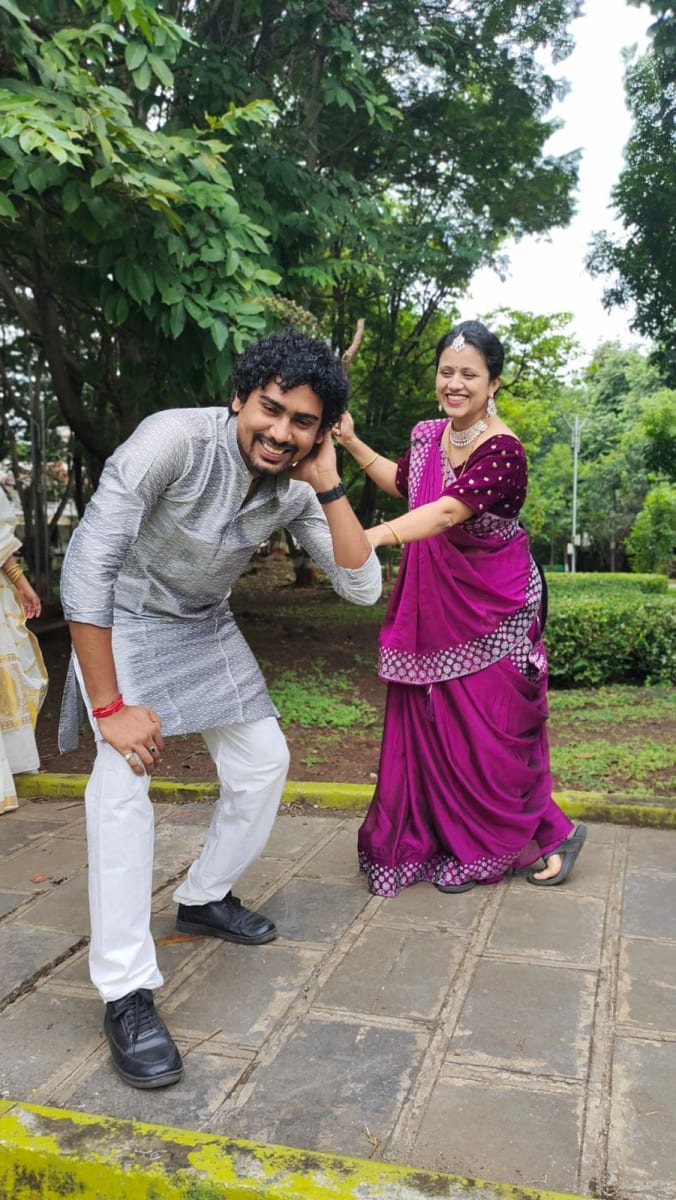 Sagar in a grey kurta laughing as a colleague in a purple saree playfully tugs his ear