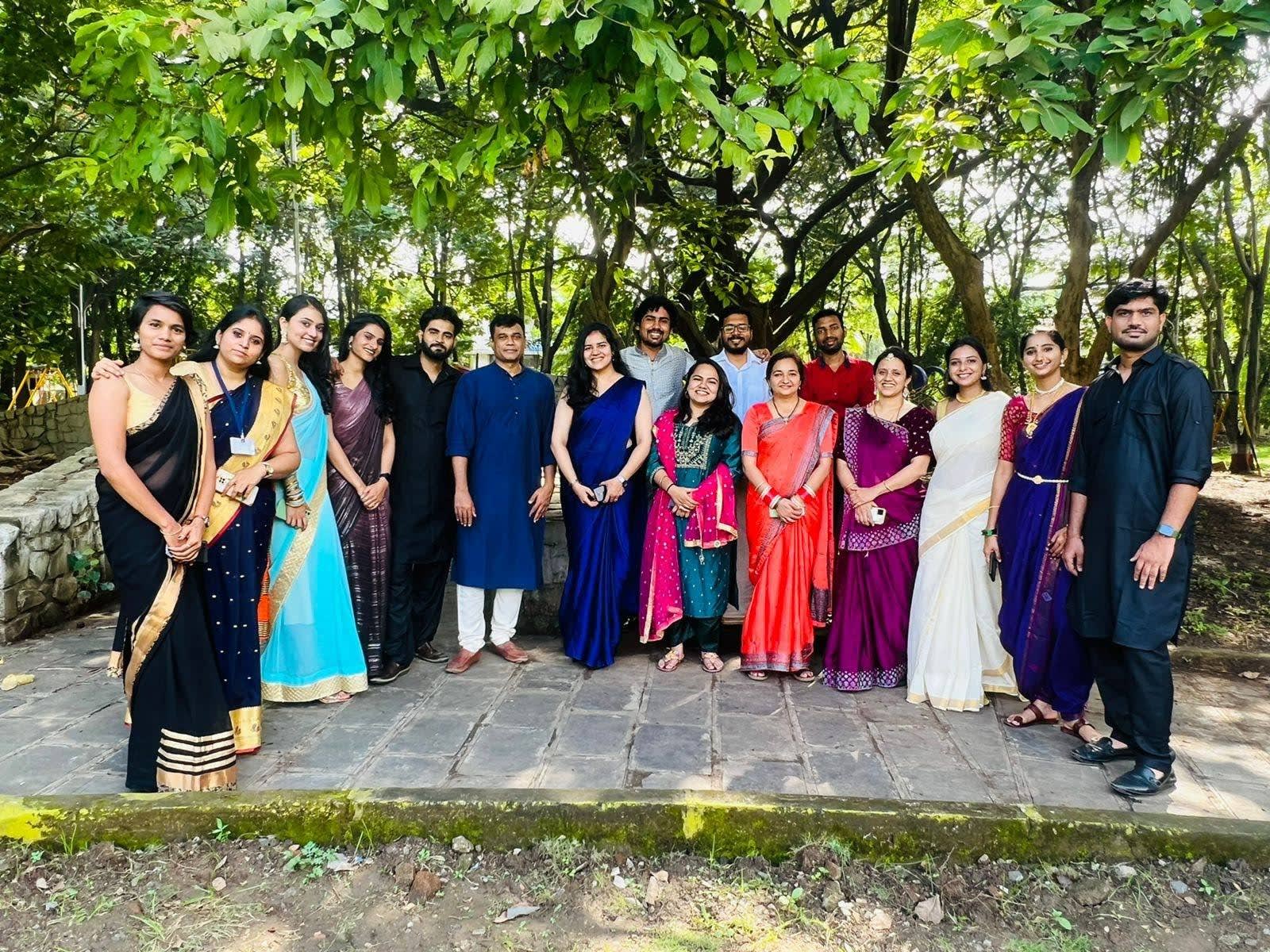 A large group of colleagues in sarees and kurtas standing together under trees