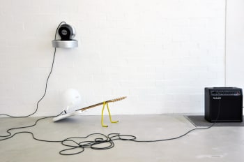 een gitaar met daarop een opgeblazen handschoen met een versterker en een ventilator tegen de muur 