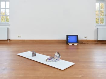 Beeldbuis TV staat tegen de muur en geeft een blauw scherm voor op licht een wit grijze plaat. maar daarop 2 op zich zelf staande abstracten werken.