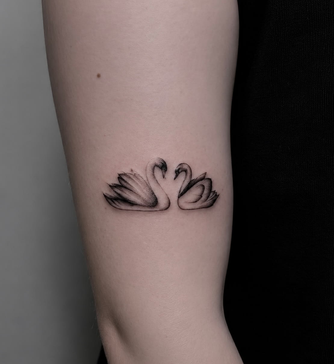 Fineline tatuaż dwóch łabędzi tworzących serce na ramieniu — Parvata Tattoo Wrocław