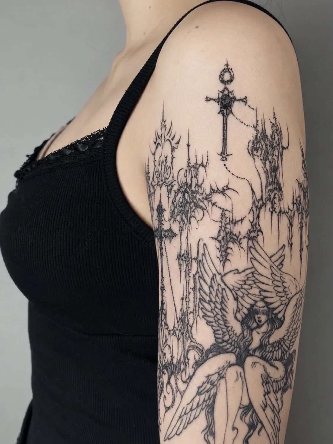 Tatuaż przedstawiający anioła w otoczeniu gotyckich wież i krzyży w stylu blackwork na ramieniu.