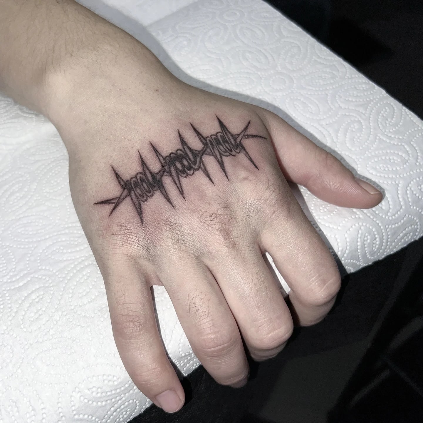 Tatuaż z drutem kolczastym wykonany w stylu blackwork na zewnętrznej stronie dłoni.