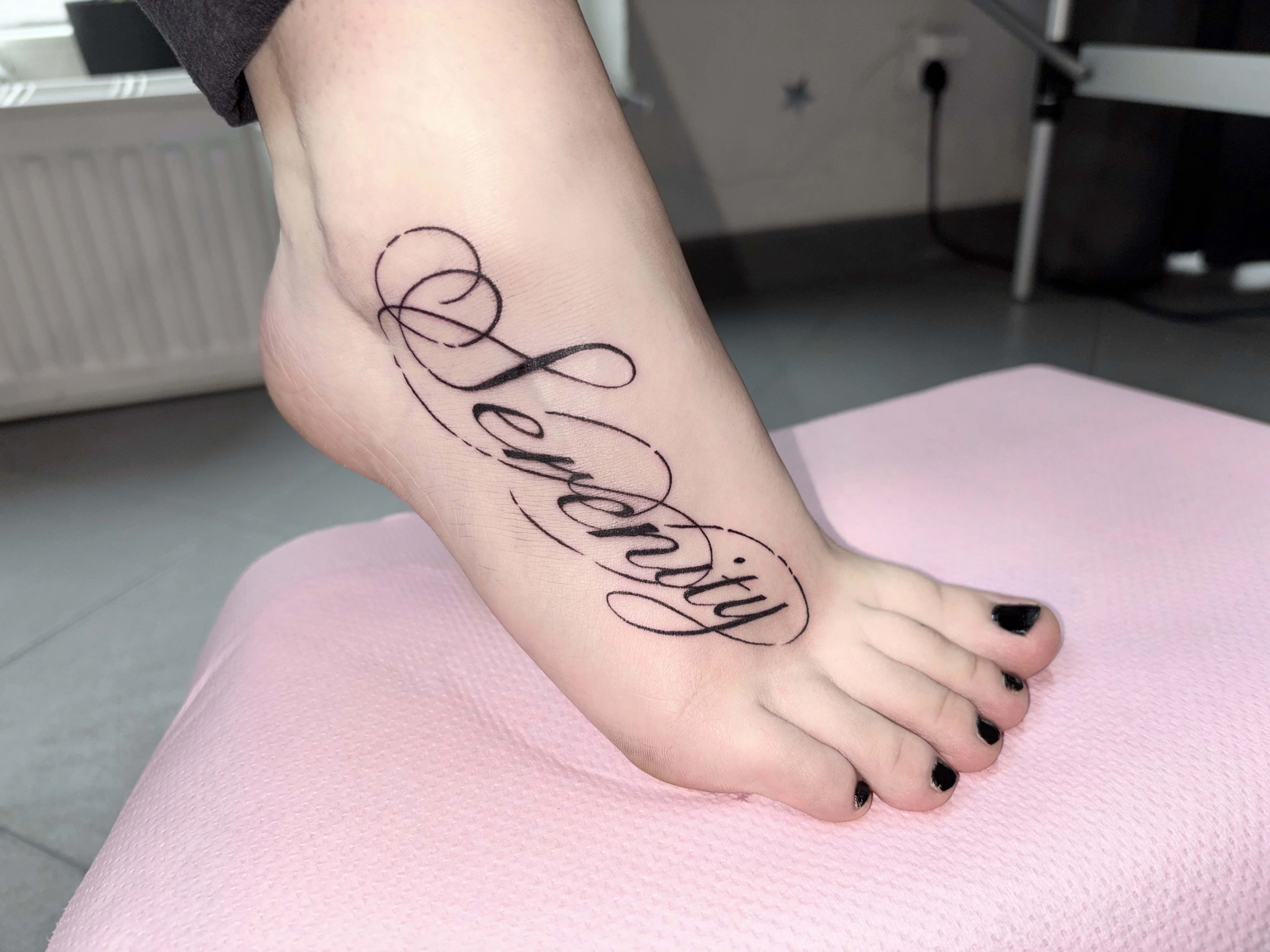 Tatuaje con la palabra «Serenity» en una cursiva fluida en el pie.