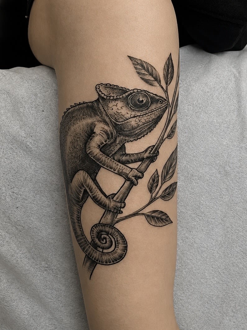 Kameleon wykonany w technice dotwork, wspinający się po gałęzi z liśćmi na przedramieniu.