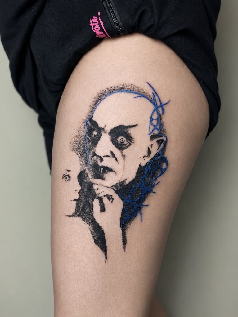 Tatuaż przedstawiający portret Nosferatu w stylu dotwork z niebieskimi elementami cybersigilism na udzie.