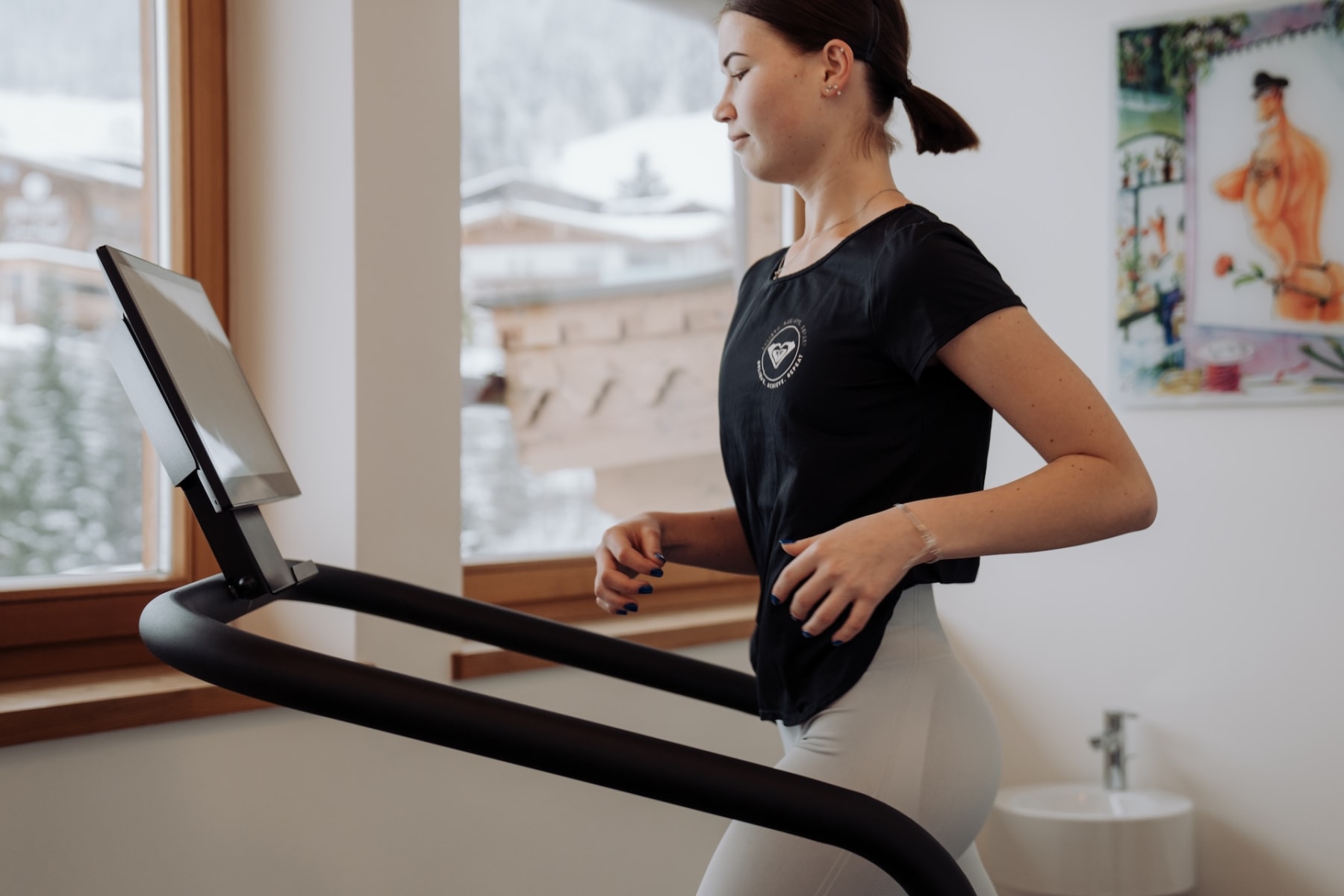 Eine Person joggt auf einem Laufband im Glemmtalerhof in Hinterglemm mit Blick auf die Winterlandschaft.