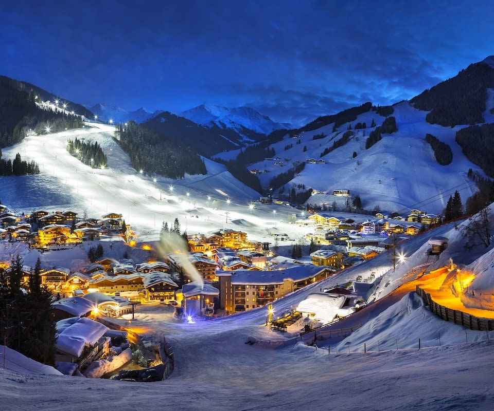 Der winterliche Glemmtalerhof in Hinterglemm strahlt in der Nacht, umgeben von schneebedeckten Bergen und Lichtern.