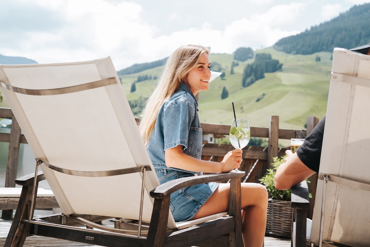 A woman enjoys a drink on a terrace with stunning views of the Glemmtal in Hinterglemm. Relaxation and nature combine.