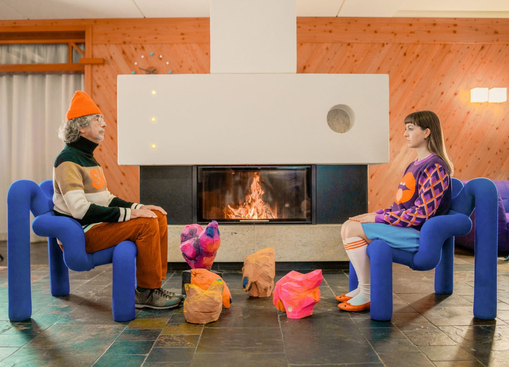 Ein Mann und eine Frau sitzen in modernen Stühlen vor einem Kamin im Glemmtalerhof in Hinterglemm.