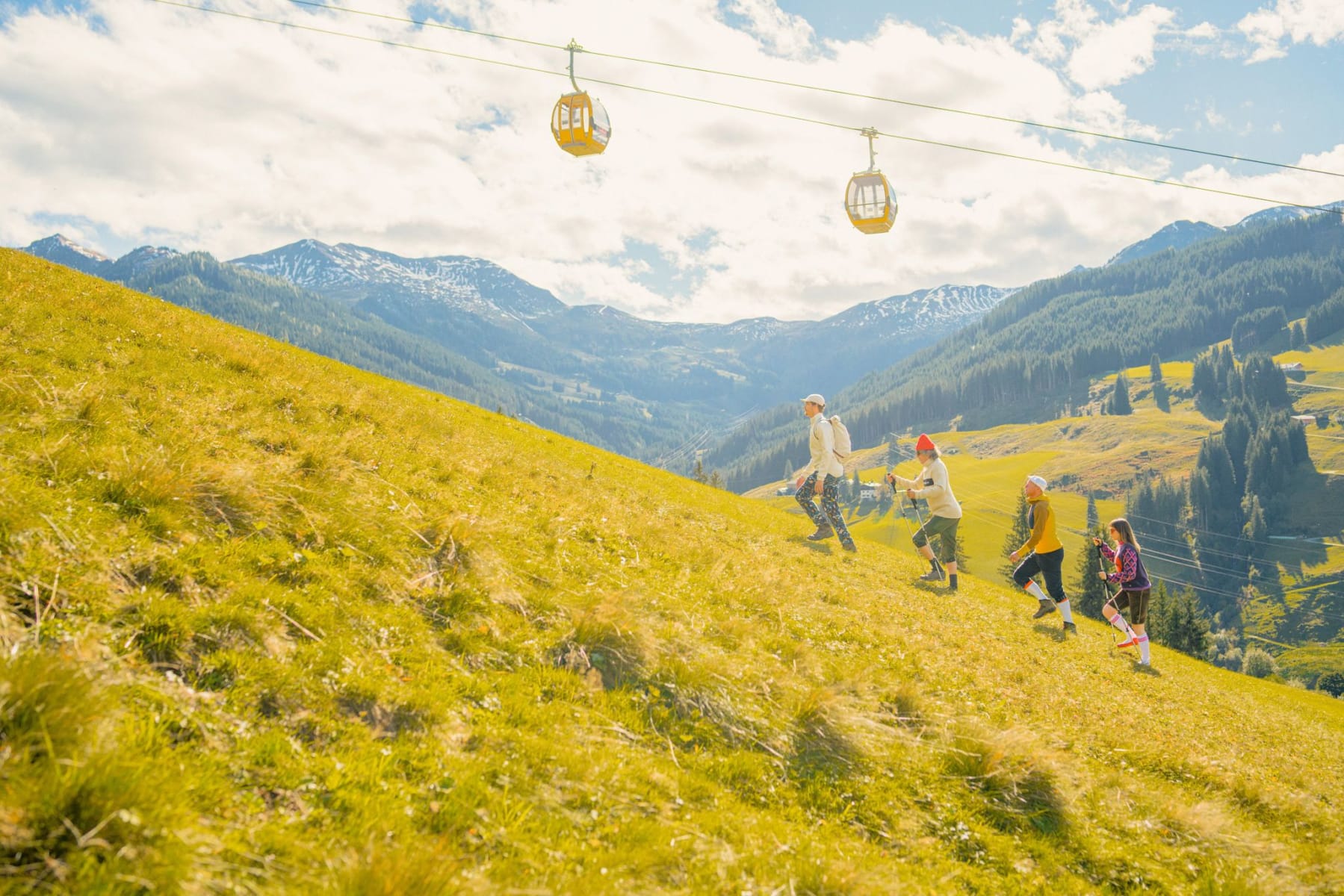 Familie wandert auf einer Wiese im Glemmtal, mit Seilbahnen im Hintergrund.