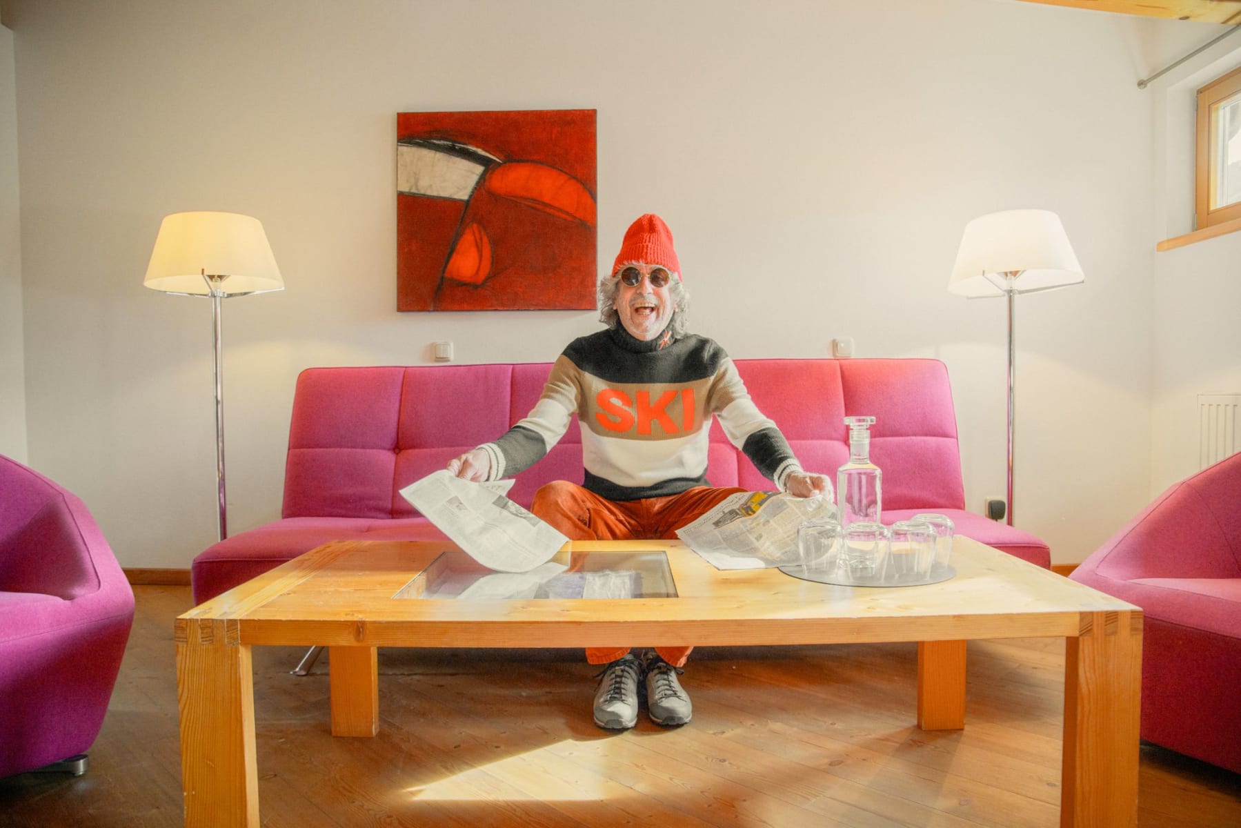 Ein fröhlicher Mann sitzt im Glemmtalerhof, umgeben von lila Sofas und bereitet sich auf das Skifahren vor.
