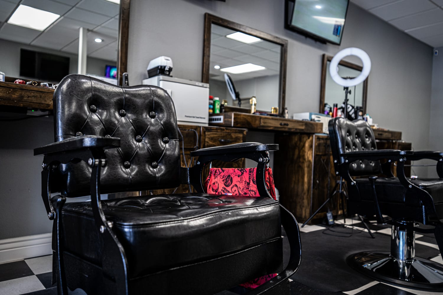 A pair of leather chairs face away from a barber's counter top. A towel is draped over the armrest of the first chair.