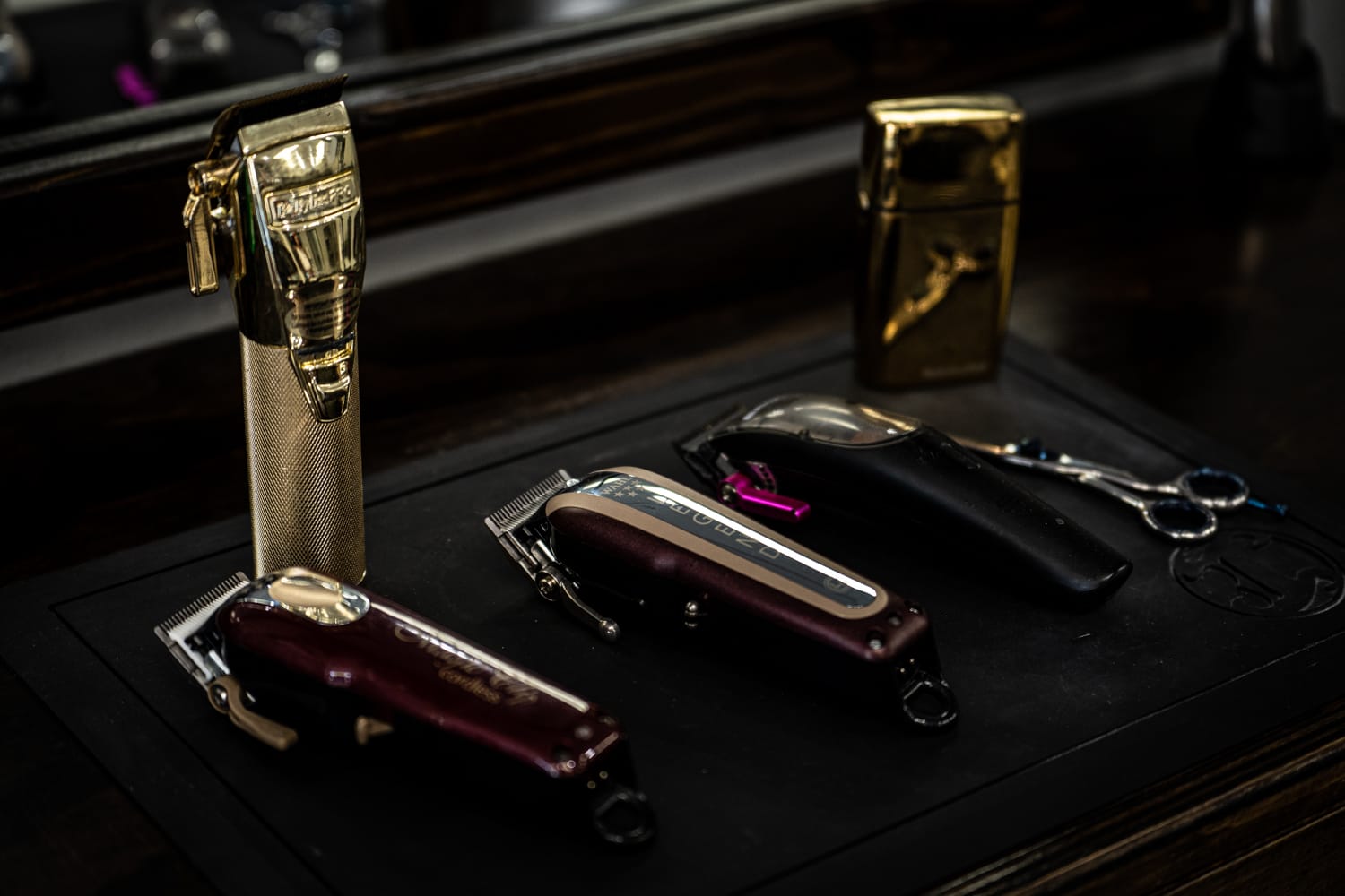 Three electric razors are organized in a row against a dark background. Next to them lie a pair of scissors.