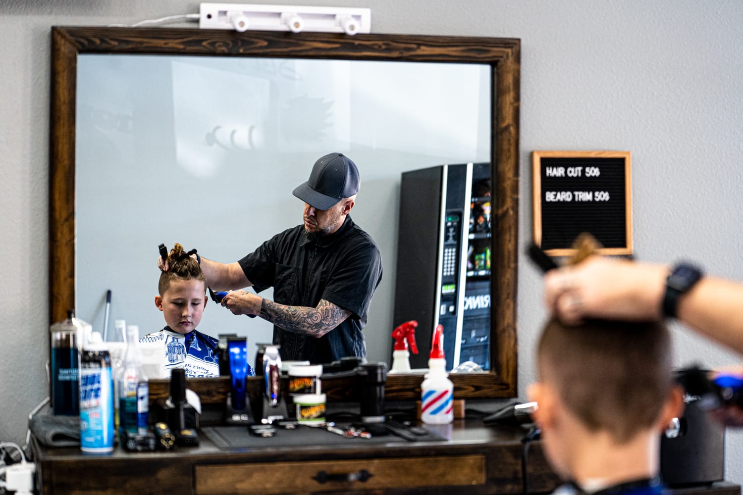 Viewed from a mirror reflection, a boy sits in a chair while the barber gives a haircut.