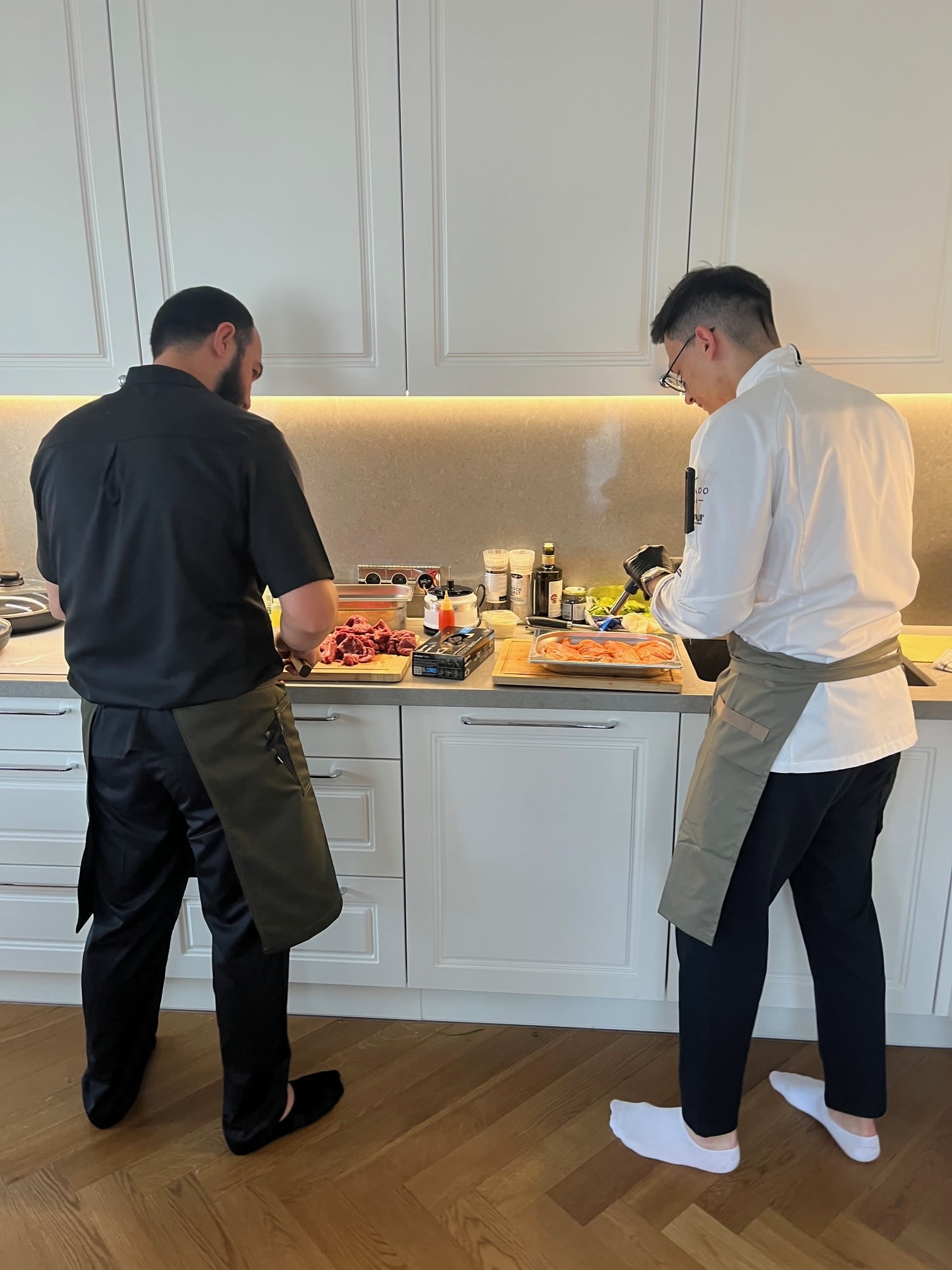 Two private chefs preparing ingredients and cooking in a modern home kitchen before a private dining event