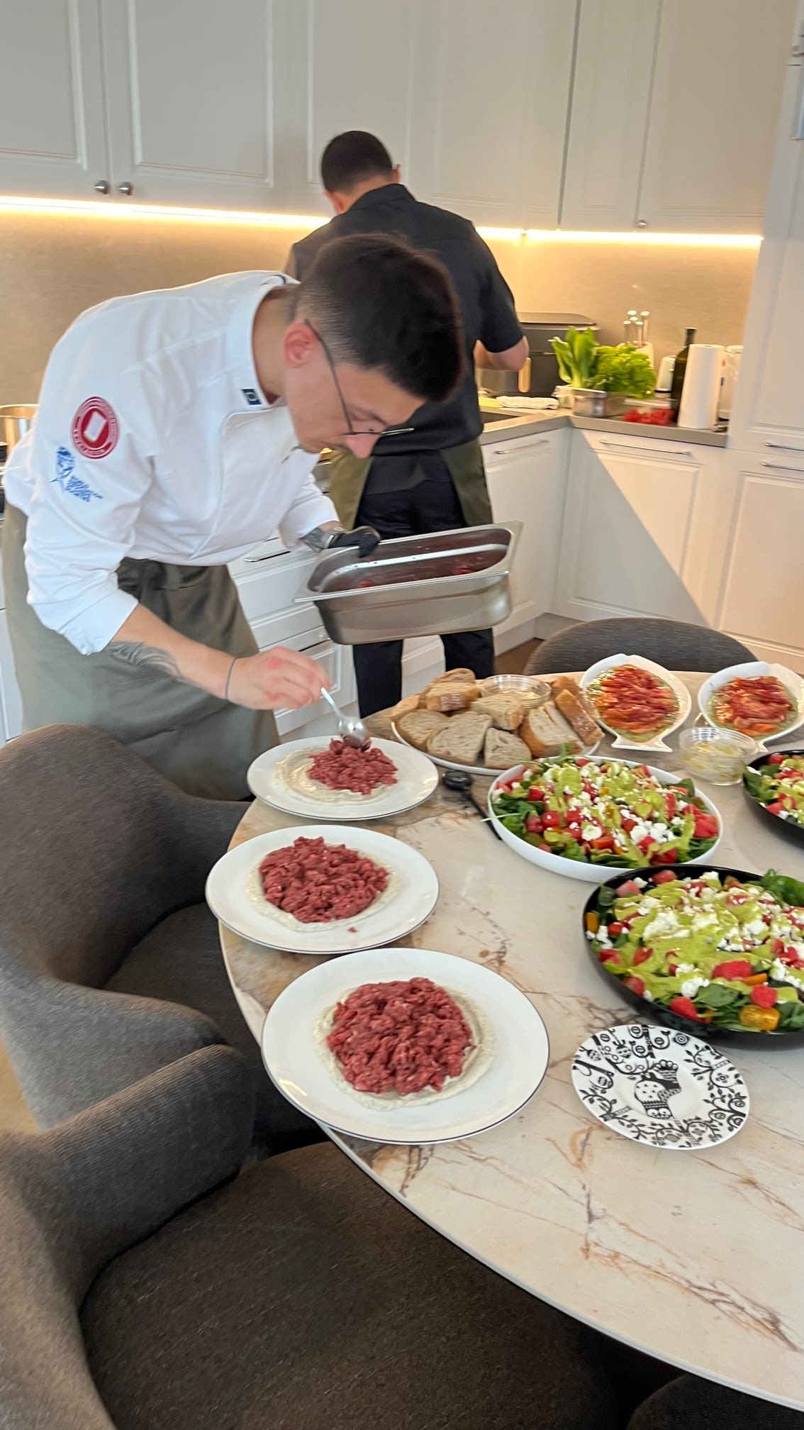 Private chef plating gourmet beef tartare while preparing a multi-course meal for guests in a private home