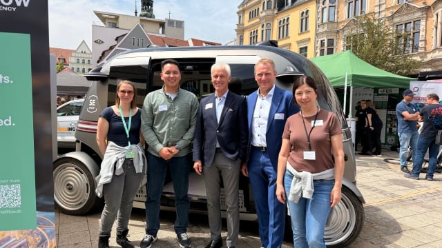 FDTech colleagues and guests standing in front of an autonomous shuttle on the main market square in Zwickau during the SAM Symposium 2026.