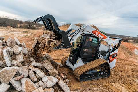 A Bobcat T76 Compact Track Loader Moves Rocks Using an Industrial Grapple Attachment
