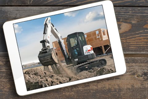 Bobcat E26 Compact Excavator with a Bucket Full of Dirt Near a Dirt Pile and an Operator Inside the Cab