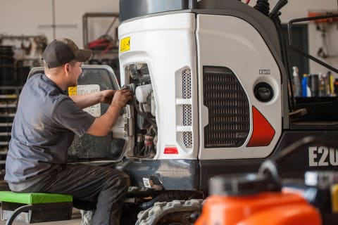 A service technician inspects the engine compartment on an E20 compact excavator.