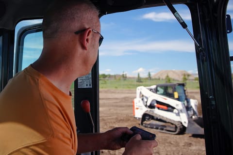A Bobcat operator using max control remote operation to move his equipment on the jobsite. 
