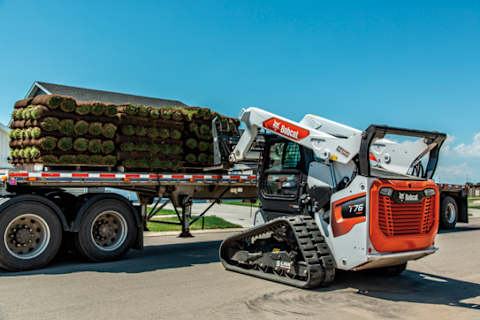 A Bobcat T76 Compact Track Loader With Pallet Forks Lifts a Stack of Turf