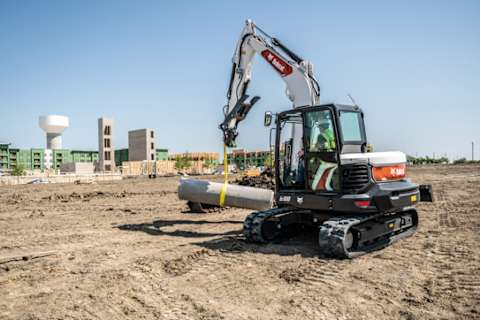 A Bobcat E88 Compact Excavator Moving a Cement Pipe on a Jobsite