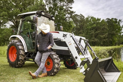 Justin Moore sits against the front tire of his Bobcat compact tractor. 