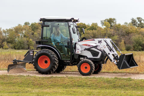 A Bobcat compact tractor with angle blade implement levels a gravel road.