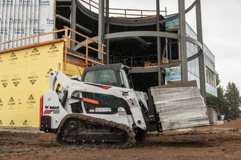 Bobcat T595 compact track loader carrying material across a construction site with pallet fork attachment