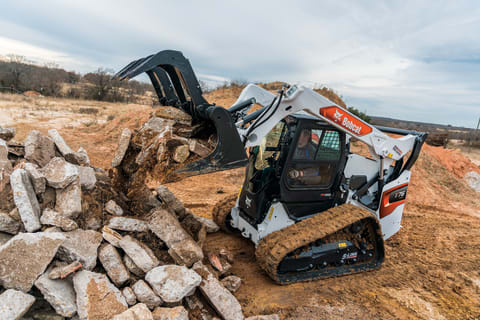 A Bobcat T76 Compact Track Loader Dumps Concrete Chunks Into a Pile With the Grapple Attachment