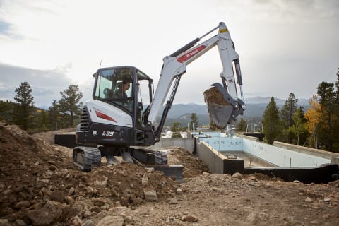 A Bobcat Compact Excavator Lifting a Bucketful of Dirt While Digging Around a Foundation