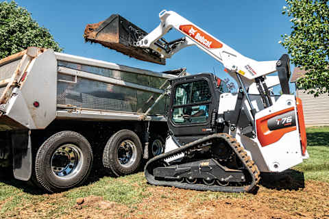 A T76 Compact Track Loader Dumps Dirt Into the Bed of a Dump Truck