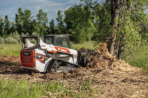 Bobcat T76 compact track loader moving mulch with a grapple attachment.