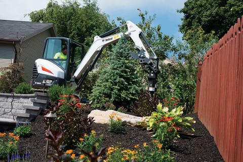 Landscaper Using Bobcat E32 Mini Excavator With Auger Attachment In Backyard Project