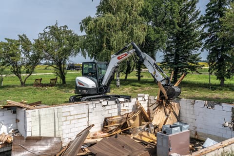Operator Using Bobcat E60 Mini Excavator With Clamp Attachment To Move Debris On Demolition Site