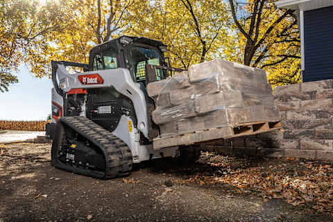 A Bobcat T66 Compact Track Loader Moves Palletized Landscaping Rocks Using a Pallet Fork Attachment