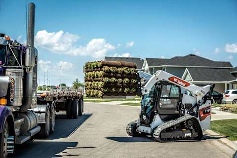 Bobcat S76 loader with pallet fork transporting materials at residential site