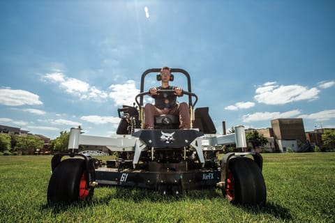 A Low-Angle Shot of an Operator on a Zero-Turn Mower Cutting Grass and Driving Into the Foreground.