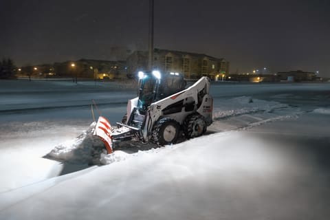 Cargadora compacta Bobcat S740 empujando nieve con una cuchilla. 